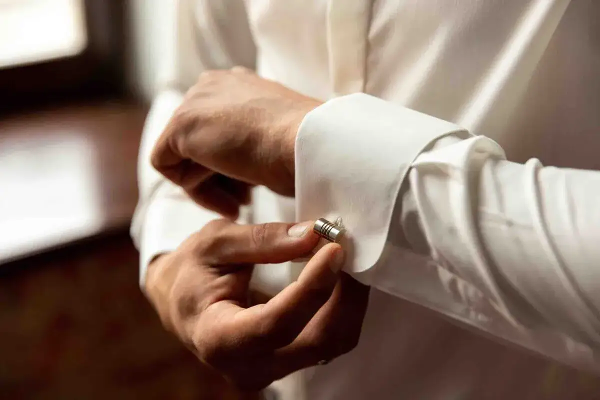 Uomo che allaccia un gemello a una camicia doppio polsino bianca. Dettaglio elegante per un look impeccabile.