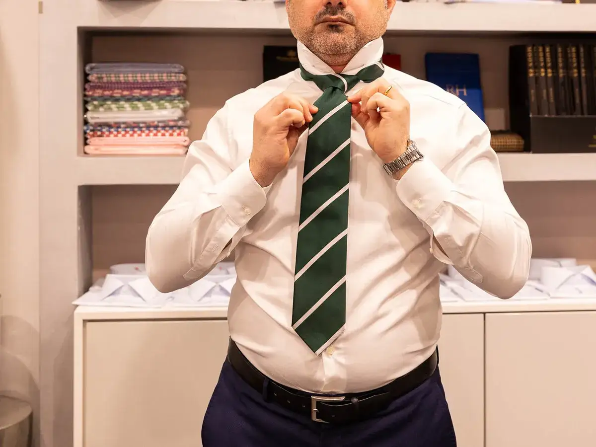 Uomo che sistema la cravatta verde a righe, mostrando la corretta lunghezza.