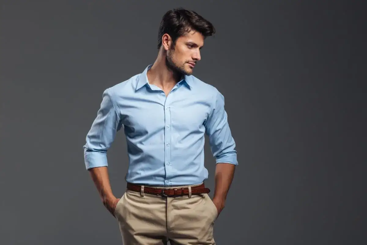 Uomo con camicia azzurra e pantaloni beige, mani nelle tasche, sguardo pensieroso.