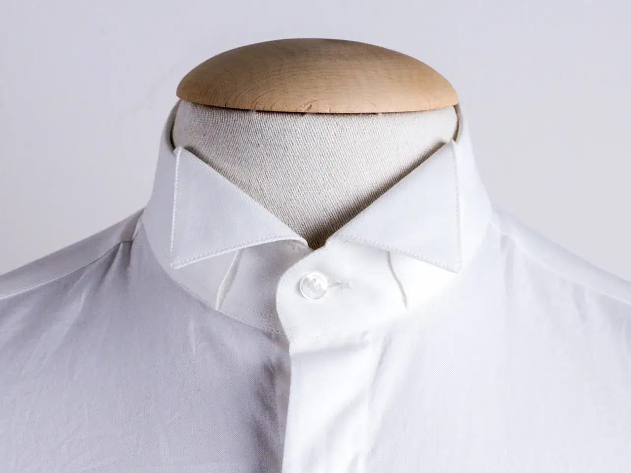 Primo piano di un colletto bianco da camicia su un manichino, che ne illustra il significato sartoriale e la forma elegante.