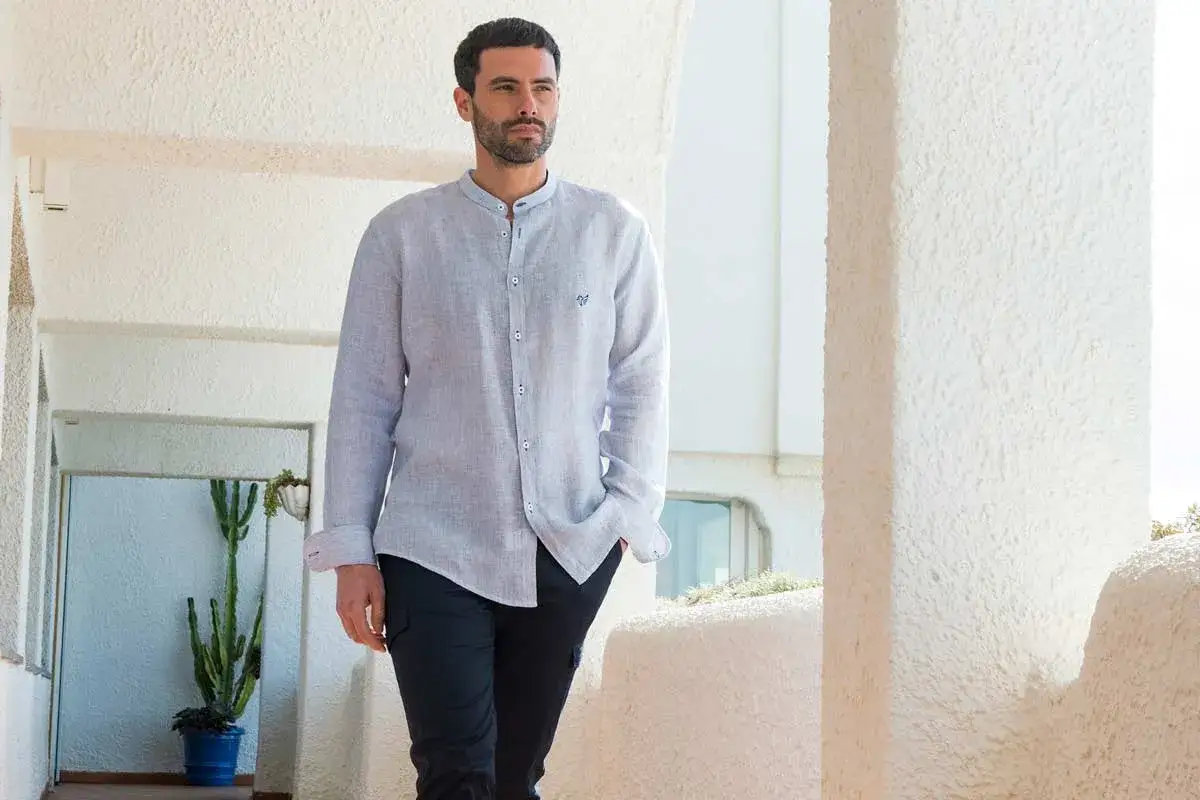 Uomo con camicia di lino azzurra sbottonata, che si mette dentro o fuori, con pantalone scuro.
