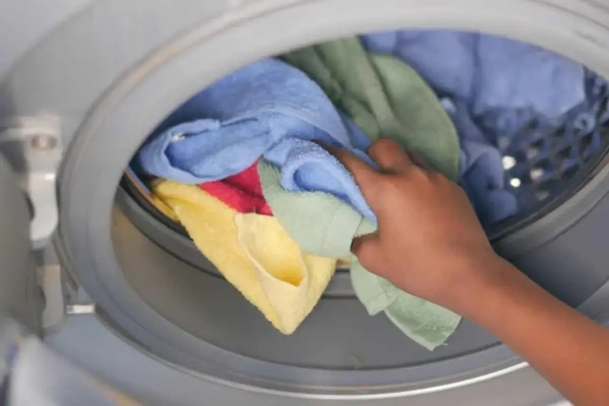 Mano inserisce strofinacci colorati nella lavatrice. Il lavaggio in lavatrice a 60 gradi igienizza a fondo.