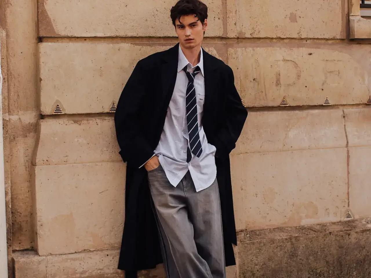 Giovane uomo con cappotto nero, camicia a righe e cravatta, jeans grigi. Un esempio di colori da abbinare al grigio scuro abbigliamento.