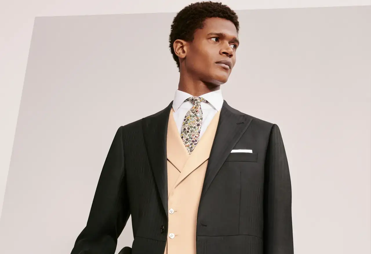 Uomo con completo scuro, gilet color pesca e cravatta floreale con nodo mezzo Windsor.