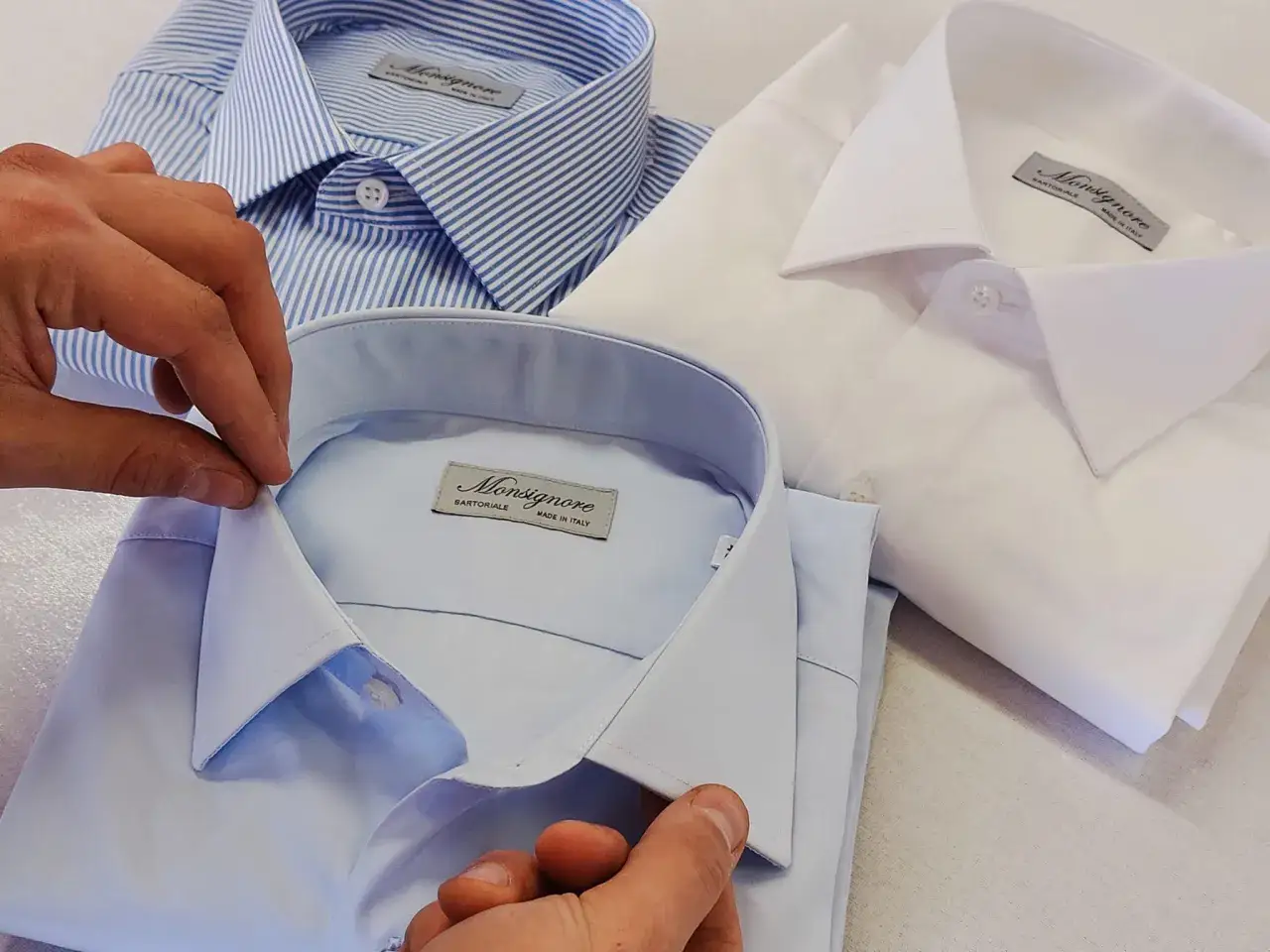 Tre camicie da uomo: una a righe blu, una azzurra e una bianca. La camicia personalizzata uomo &egrave; un capo sartoriale di alta qualit&agrave;.
