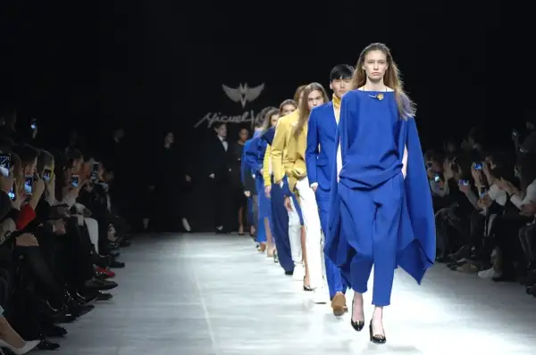 Sfilata di moda con modelli in abbinamento blu elettrico e bianco. Il pubblico scatta foto con i cellulari.