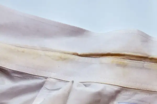 Colletto di camicia con evidenti macchie gialle, simili a quelle che si formano su asciugamani colorati dopo l'uso.