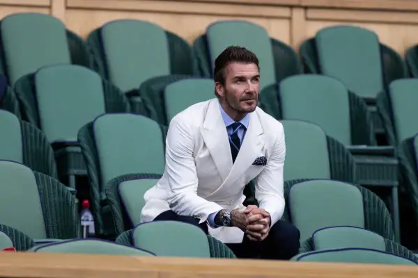 David Beckham in una giacca bianca uomo abbinamento impeccabile, con camicia azzurra e cravatta blu, siede tra le tribune verdi di Wimbledon.