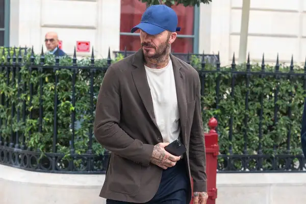 Uomo con abbinamento blu e marrone: blazer marrone, t-shirt bianca, cappellino blu e pantaloni scuri.