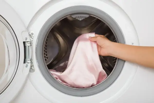 Mano inserisce un capo colorato in lavatrice. Ecco come lavare i capi colorati la prima volta per evitare che stingano.