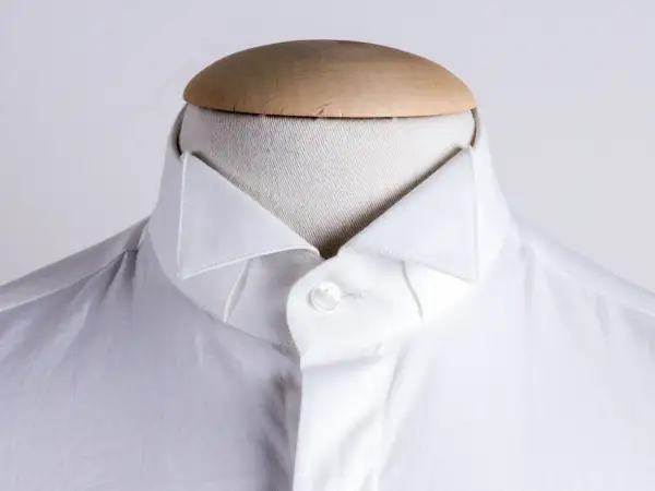 Dettaglio di una camicia bianca da uomo con un elegante camicia con colletto a punta, abbottonata su un manichino.