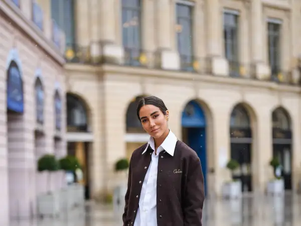 Donna con outfit camicia bianca inverno, giacca marrone e sfondo di un edificio parigino.