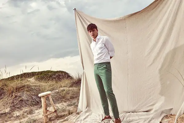 Uomo con camicia bianca e abbinamento pantalone verde su sfondo naturale.