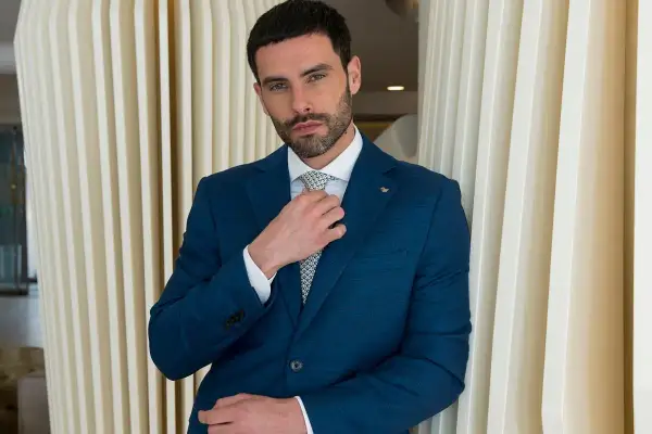 Uomo in abito blu che sistema la cravatta, un esempio di come si mette cravatta con stile.