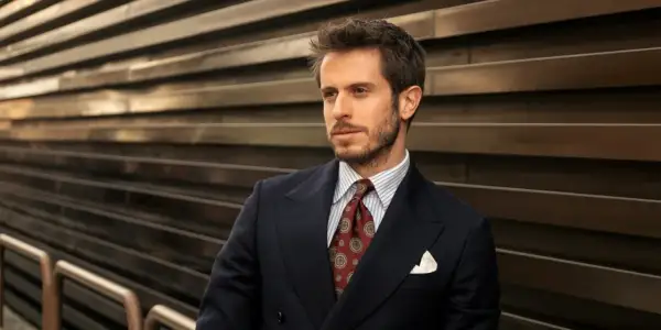 Uomo con abito blu, camicia a righe e cravatta verde con fantasia. Sguardo pensieroso.