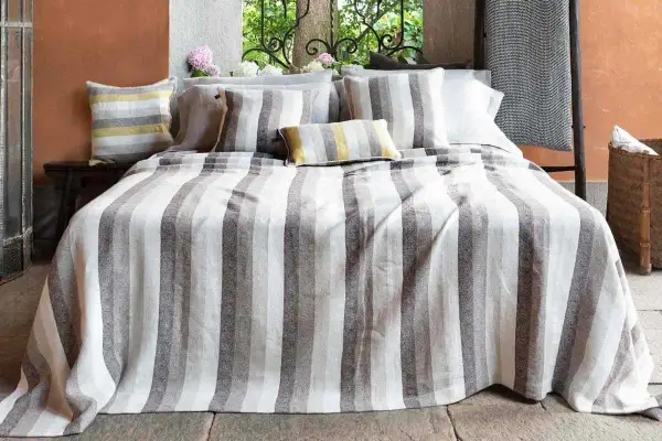 Letto con biancheria a righe grigie e bianche, cuscini coordinati. Un'immagine che ispira su come lavare il lino per mantenerlo morbido.