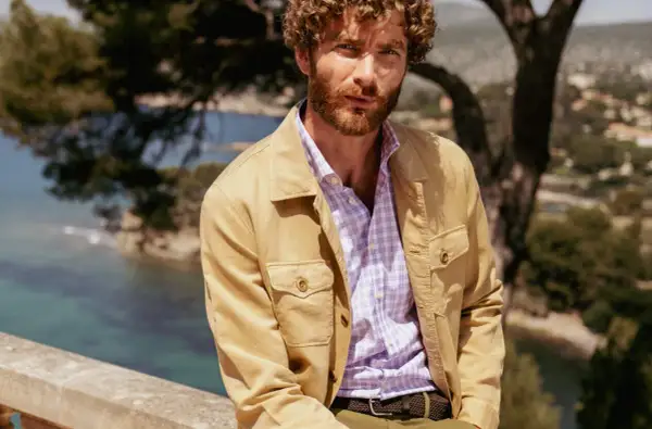 Uomo con camicia a quadri viola e giacca color sabbia, un'idea di cosa mettere sopra una camicia per un look casual chic.