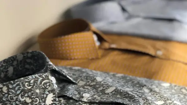 Dettaglio di camicie con fantasie diverse. Una grigia floreale, una senape a pois e una azzurra. Perfette per ogni occasione, con un fermamaniche camicia per un tocco di stile.