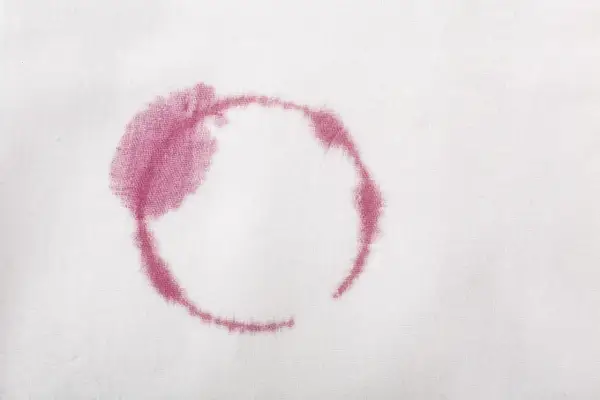 Macchie rosse sui vestiti dopo lavaggio in lavatrice, un alone circolare di vino su tessuto bianco.