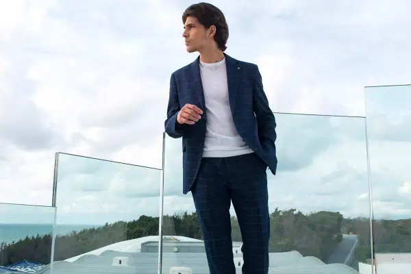 Uomo con completo a quadri blu scuro, maglia bianca. Colori che si abbinano con il blu scuro uomo, su una terrazza con vista mare.
