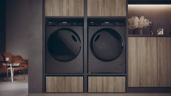 Due asciugatrici nere affiancate, con un cassetto in legno sotto ciascuna. Le lenzuola in asciugatrice sono pronte per essere piegate.