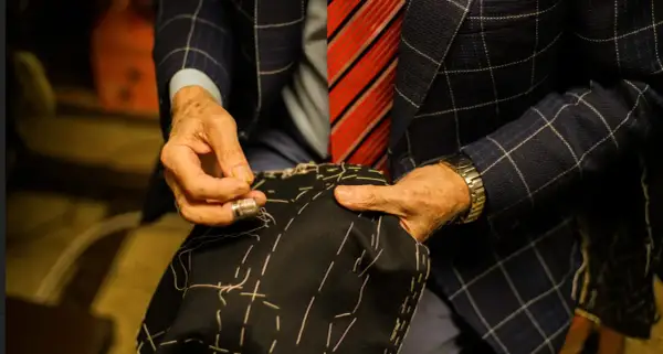 Sarto esperto cuce a mano un tessuto scuro, mostrando i diversi tipi di polsini camicia e la cura artigianale.